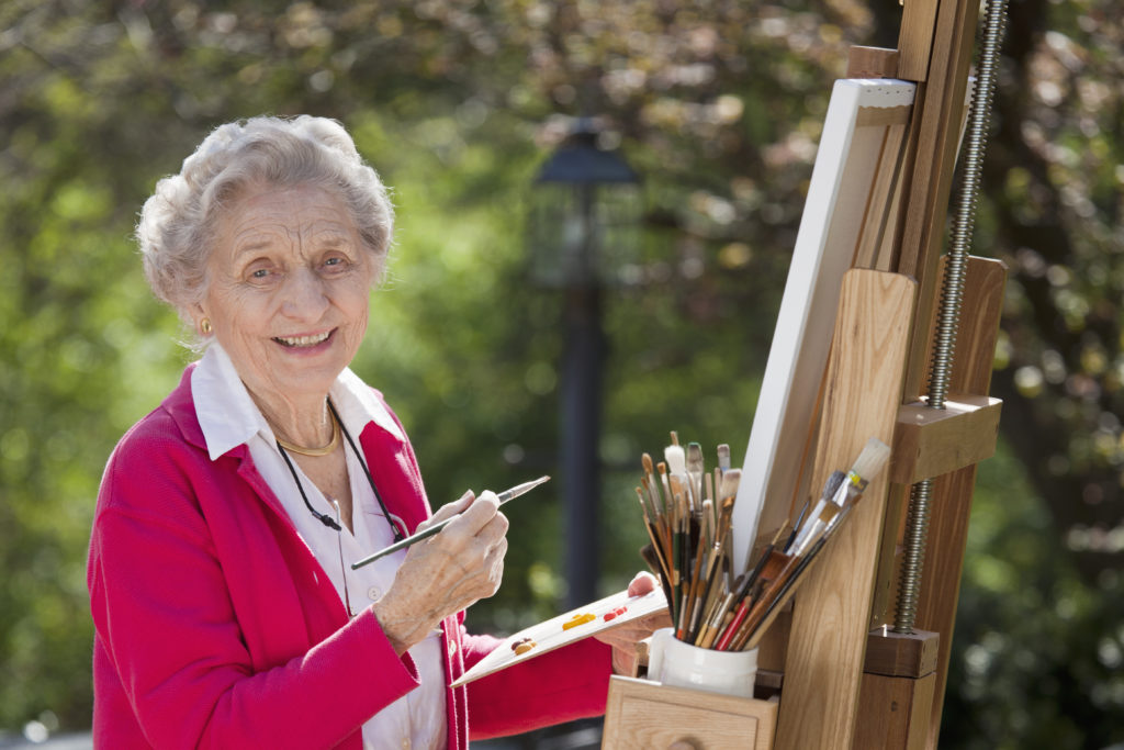 Smiling senior woman sitting outdoors painting.