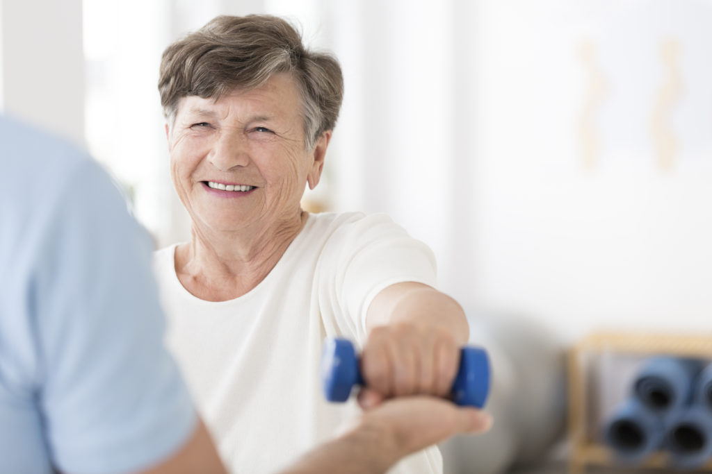 Happy senior woman exercising arms with small weight.